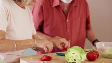 Mutfakta sebze doğrayan yaşlı bir çift emekliliklerinin ve sağlıklı yaşamlarının tadını çıkarıyor.