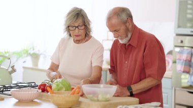 Yaşlı çift havuç ve diğer sebzeleri kesiyor, birlikte çalışarak mutfaklarında sağlıklı bir yemek hazırlıyorlar.