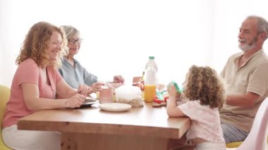 Üç nesildir evde sağlıklı bir kahvaltı yapan neşeli bir aile. Büyük anne, büyük baba ve küçük bir kız mutlu bir anı paylaşıyorlar.