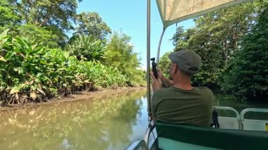 Nehir kenarındaki bir safaride erkek turist, yoğun mangrov ormanını ve Kosta Rika 'daki verimli tropikal ormanı filme alıyor.
