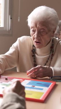 Beyaz saçlı kadın ve erkek emeklilerin yavaş çekimde boş zamanlarında masada oturup masa başında oyun oynamaları.