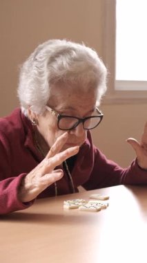 Yaşlı erkek ve kadın arkadaşlar günlük kıyafetleriyle masada domino oynarken huzurevinde vakit geçiriyorlar.