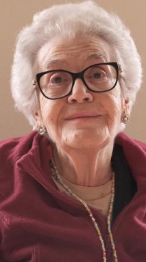 Huzurevinde konuşurken gözlük takan kısa gri saçlı yaşlı kadının portresi.