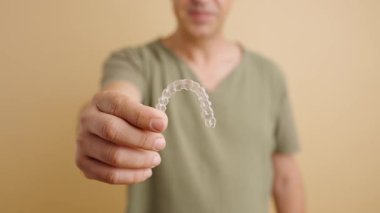 Elinde şeffaf plastik bir hizalayıcı tutan gülümseyen adam. Diş düzeltme ve düzeltme için görünmez diş telleriyle ortodontik tedavi