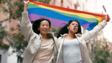 Gurur gününü kutlarken elinde gökkuşağı bayrağı olan aynı cinsten iki mutlu genç kadın. Güzel lezbiyen çift gülümser ve güler.