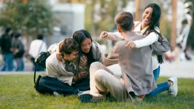 Güzel bir şehir parkında çimlerin üzerinde otururken birbirini sıcak bir kucaklaşmayla selamlayan çok kültürlü bir arkadaş grubu.