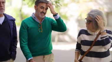 Üst düzey karı koca bir caddede yürüyor ve konuşuyor. Adam öfkeyle bir şeyi açıklamaya çalışıyor, anlaşmazlık içinde.