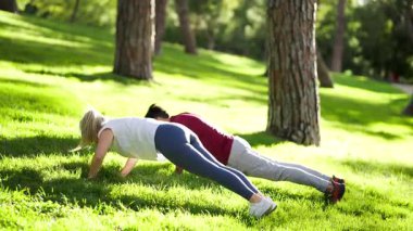 Atletik erkek ve kadın yemyeşil çimlerde senkronize şınav çekiyorlar. Açık hava sporu ve spor yaşam tarzı konsepti