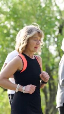 Yetişkin bir kadın parkta sabah koşusundan zevk alıyor. Bu aktif son sınıf öğrencisi sağlıklı bir yaşam tarzı sürdürmek için kardiyo çalışmasına odaklanmış. Dikey