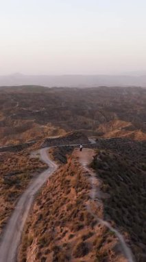 Günbatımında İspanya 'daki Gorafe Çölü' nün dolambaçlı yollarına bakan uçurumun kenarında duran yalnız bir insanın hava manzarası.