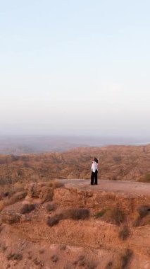 Uçurumun kenarında kollarını kaldırmış dans eden uzun saçlı sakin bir kadın. İspanya 'daki gorafe çölü çorak topraklarının güzel geniş manzarası.