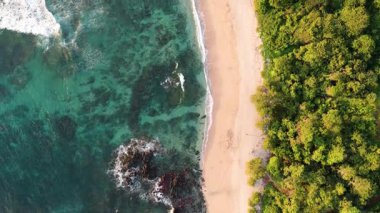 Kosta Rika 'daki el değmemiş beyaz kumlu plajın uçucu perspektifi. Kristal berrak turkuaz su, yemyeşil tropikal ormanla buluşur.