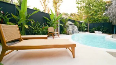 Modern şezlongları olan şık bir yüzme havuzu. Güzel bir tropikal bahçesi ve küçük bir şelalesi olan özel bir villada huzurlu bir ortam.