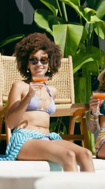 Yaz tatilinin tadını çıkaran iki şık kadın. Dostlar tropikal bir havuz partisinde ferahlatıcı bir içecekle rahatlıyorlar. Dikey