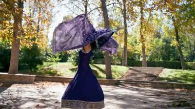 Güneşli bir parkta geleneksel Hint dansı yapan güzel bir genç kadın. Akan mor bir sariyle gülümseyen ve dönen zarif bir dansçı.