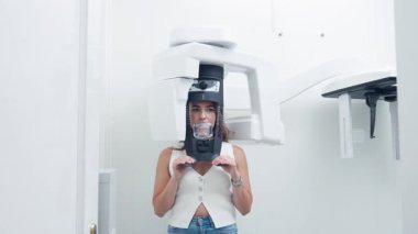 Modern bir diş panoramik röntgen makinesi, parlak ve temiz bir klinik ortamında başının etrafında dönerken kadın hasta sabit duruyor.
