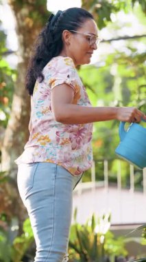 Neşeli yaşlı kadın elinde mavi bir su bidonu tutuyor ve bitkileriyle ilgileniyor. Bahçıvanlık hobisiyle meşgul olan mutlu bir son sınıf öğrencisi.