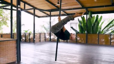 Geniş, parlak bir stüdyoda çağdaş bir direk dansı sırasında inanılmaz esneklik ve kontrol sergileyen güçlü bir atletik adam.