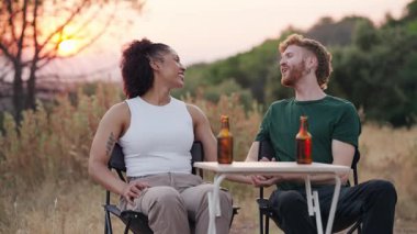 Genç melez çift dışarıda romantik bir buluşmanın tadını çıkarıyor. Mutlu bir adam ve kadın gün batımında gülüyor, konuşuyor ve el ele tutuşuyorlar.