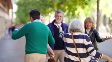 Mutlu bir son sınıf arkadaş grubu birbirlerini selamlıyor ve kucaklıyorlar. Güneşli bir günde dışarıda buluşan olgun insanların duygusal birleşmesi.