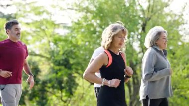 Sağlıklı bir grup olgun arkadaş parkta birlikte koşuyor. Üst düzey erkek ve kadınlar açık hava kardiyo egzersizleriyle sağlıklı bir yaşam sürdürüyorlar.