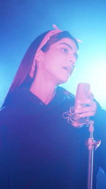 Profesyonel bir kayıt stüdyosunda şarkı söyleyen yetenekli bir bayan şarkıcı. Pembe ve mavi neon ışıklı yeni bir müzik kaydeden bir müzisyen. Dikey görüntüler