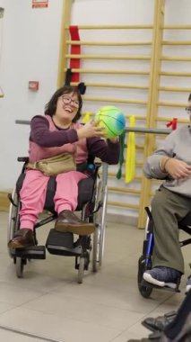 Bir grup fizyoterapi seansında tekerlekli sandalyede sakat bir şekilde top oynarken eğlenen bir grup insan.