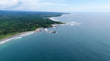 Kosta Rika Pasifik kıyıları tropikal bir plaj, yoğun yağmur ormanı ve dalgaların kıyıya vurduğu derin mavi bir okyanus sergiliyor.
