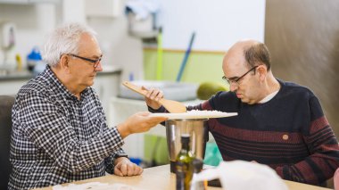 İki adam, biri engelli, mutfakta birlikte çalışıyorlar, desteklenen bir ortamda pirinç pişirmeyi öğreniyorlar.