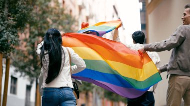 Elinde gökkuşağı bayrağı olan genç insanlar, şehir sokaklarında yürüyor, LGBTQ artı gurur ve eşitliği kutluyorlar.