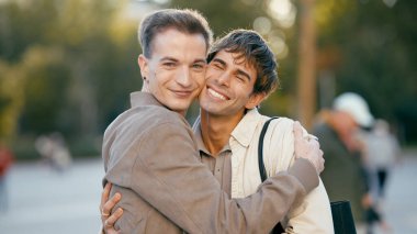 Açık havada kucaklaşan iki genç adam, sevgi, mutluluk, romantik bir ilişki ve LGBTQ artı bir halk parkında gurur gösteriyorlar.