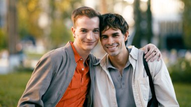 İki mutlu adam kucaklaşıyorlar, açık hava parkında birlikte vakit geçiriyorlar, yoldaşlık ve aşkı ifade ediyorlar.