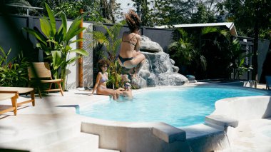 Genç arkadaşlar, yaz tatilinde tropikal bir tatil köyünde havuza atlayıp eğleniyorlar.