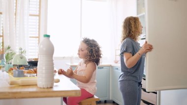 Anne buzdolabını açarken küçük kız mutfak adasında oturuyor. Birlikte sabah yemeği hazırlıyoruz.