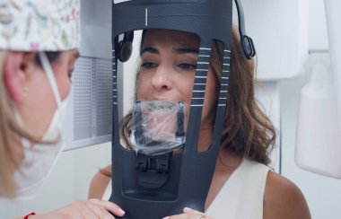 Dişçi kadın hastayı panoramik diş röntgeni için yerleştiriyor. Klinikte diş muayenesi için modern dijital teknolojiyi kullanıyor.