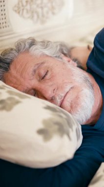 Gri saçlı, sakallı, huzur içinde uyuyan son sınıf öğrencisinin fotoğrafını çek. Yatakta dinlenen olgun bir insan. Huzurlu ve rahat. Dikey