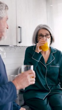 Modern mutfaklarında pijamalı, taze portakal suyu içen mutlu bir çift. Güne birlikte başlıyorlar. Dikey