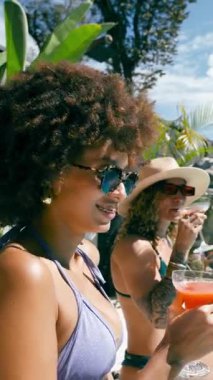 Bikinili iki güzel kadın yüzme havuzunda dinleniyor. Arkadaşlar birlikte güneşleniyor, güneşli bir günde ferahlatıcı kokteyller içiyor. Dikey