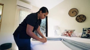 Profesyonel oda hizmetçisi yeni yapılmış bir yatakta havluyu dikkatlice katlıyor. Çalışkan konukseverlik çalışanı mükemmel oda servisi sağlıyor.