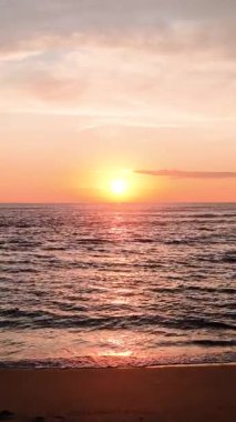 Deniz ufkunun üzerinde batan sıcak güneşin güzel manzarası. Sakin okyanus dalgaları altın akşam ışığını yansıtıyor. Dikey görüntüler