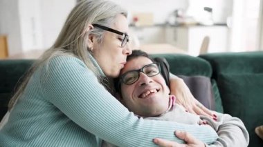 Sevgi dolu bir anne ile fiziksel durumu olan oğlu arasındaki hassas an. Onu kucaklıyor ve kanepede alnından öpüyor.