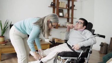 Sevgili büyük anne, evde tekerlekli sandalyedeki yetişkin oğluna spina bifida konusunda dikkatli bir şekilde yardım ediyor. Aile hayatı ve evde bakım kavramı