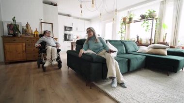 Tekerlekli sandalyedeki genç bir adam televizyon izlemek için kanepede annesine katılıyor. Oturma odasında birlikte geçirdiğimiz kaliteli aile zamanı.