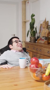 Fiziksel durumu iyi olan neşeli bir genç adam mutlu bir anın tadını çıkarıyor. Gülüyor ve tahta masada başka bir insana beşlik çakıyor.