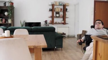 Fiziksel durumu olan bir adam, modern, parlak oturma odasında hareket etmek için motorlu sandalye kullanıyor.