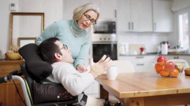 Destekleyici anne, Spina Bifida yüzünden tekerlekli sandalye kullanan yetişkin oğluna yardım ediyor. Aile anlarını sevmek, özen ve günlük hayatı göstermek.