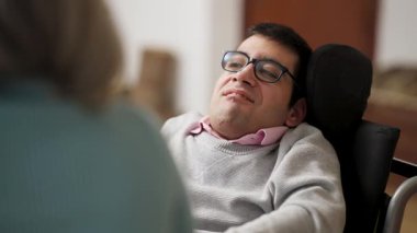 Fiziksel engelli genç bir adam tekerlekli sandalyede oturuyor, gülümsüyor ve başka biriyle konuşuyor. Otantik kapsama ve mutluluk anı
