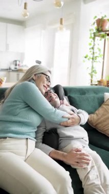 Sevgi dolu orta yaşlı bir anne, yetişkin oğlunu kanepede spina bifida ile kucaklıyor. Şefkatli aile anları evde bakım ve mutluluğu ifade eder. Dikey