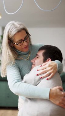 Sevgi dolu bir anne, evde fiziksel engelli bir şekilde yaşayan yetişkin oğlunu kucaklıyor. Sevgi ve derin bir bağ gösteren mutlu aile anları. Dikey