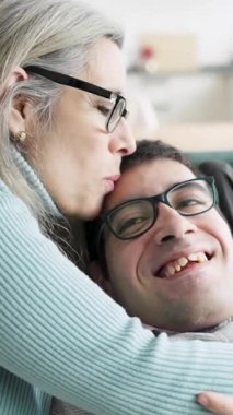 Sevgi dolu bir anne, yetişkin oğlunu fiziksel olarak kanepede kucaklıyor. Güzel bir aile sevgisi, özen ve bağ anı.